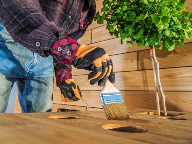 Professional contractor applying stain to a wooden deck using a paintbrush.