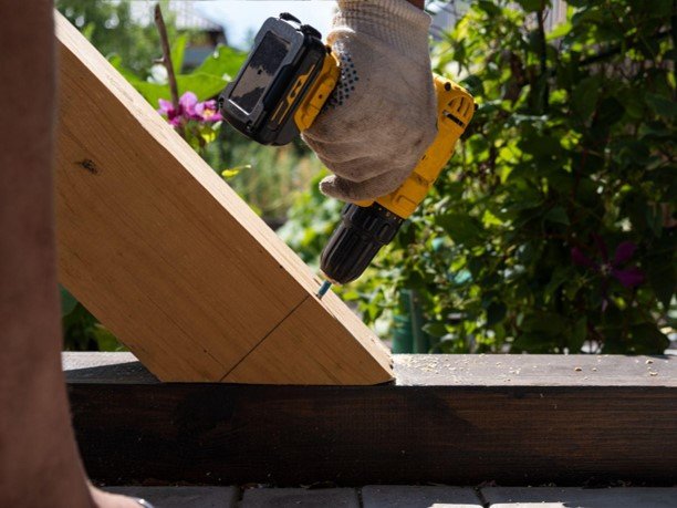 Professional contractor repairing a wooden deck with a power drill.