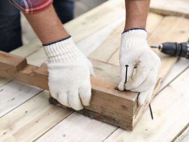 A professional working on custom deck construction holding a screw nail and a power tool to the side.