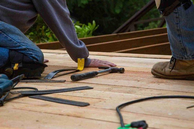 Contractors repairing wood deck boards with hand tools during a residential deck repair project.