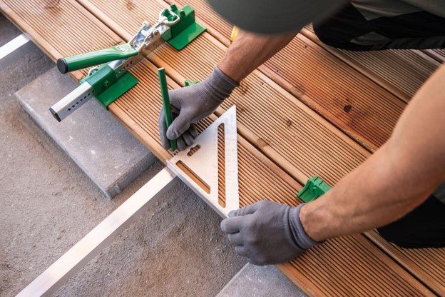 Contractor measuring and marking wood decking during a residential porch construction project.