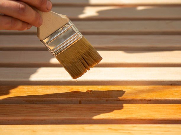 Professional applying stain to wooden deck boards with a paintbrush.